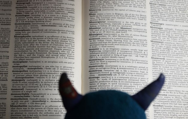 the top of Edgar's head and his horns as he is reading the dictionary, open to the page with the definition of monster, as well as a lot of other words that start with mo 